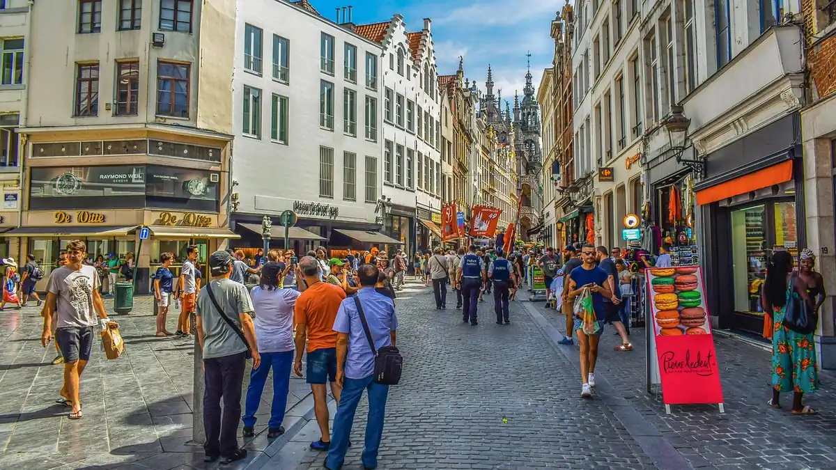 Rue commerçante du centre de Bruxelles remplie de piétons, flèche de l'hôtel de ville en arrière-plan
