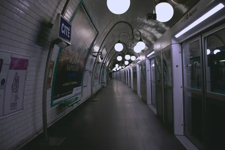 Quai désert de la station Cité à Paris, lampadaires en boule blanche et rame arrêtée derrière les portes