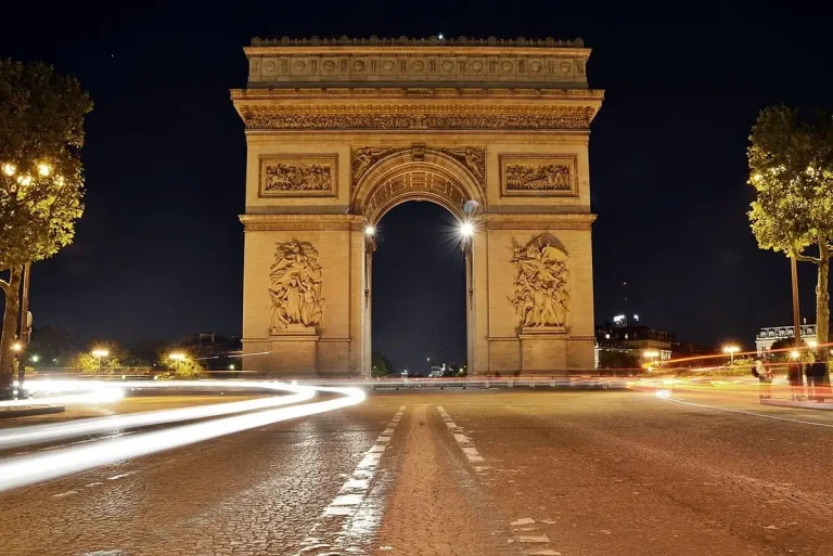 Arc de Triomphe illuminé la nuit, traînées de phares des voitures sur la place de l'Étoile au premier plan