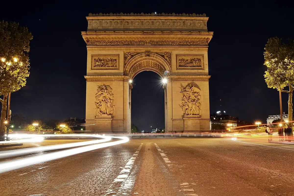 Arc de Triomphe illuminé la nuit, traînées de phares des voitures sur la place de l'Étoile au premier plan