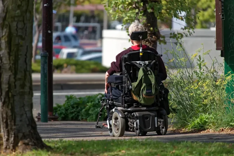 Personne âgée en fauteuil roulant électrique sur un trottoir de ville, vue de dos