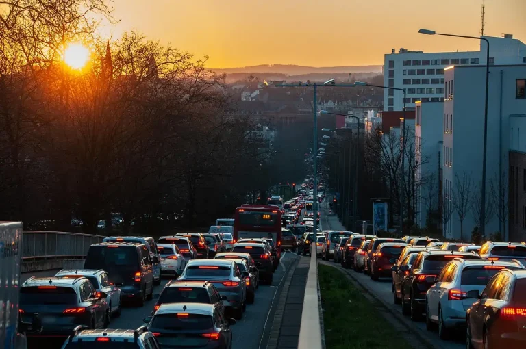 Embouteillage de voitures sur une avenue urbaine au coucher du soleil, feux arrière allumés et bus rouge au loin