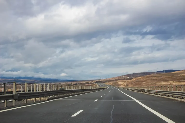 Autoroute à deux voies déserte sous un ciel nuageux, glissières de sécurité et collines au loin