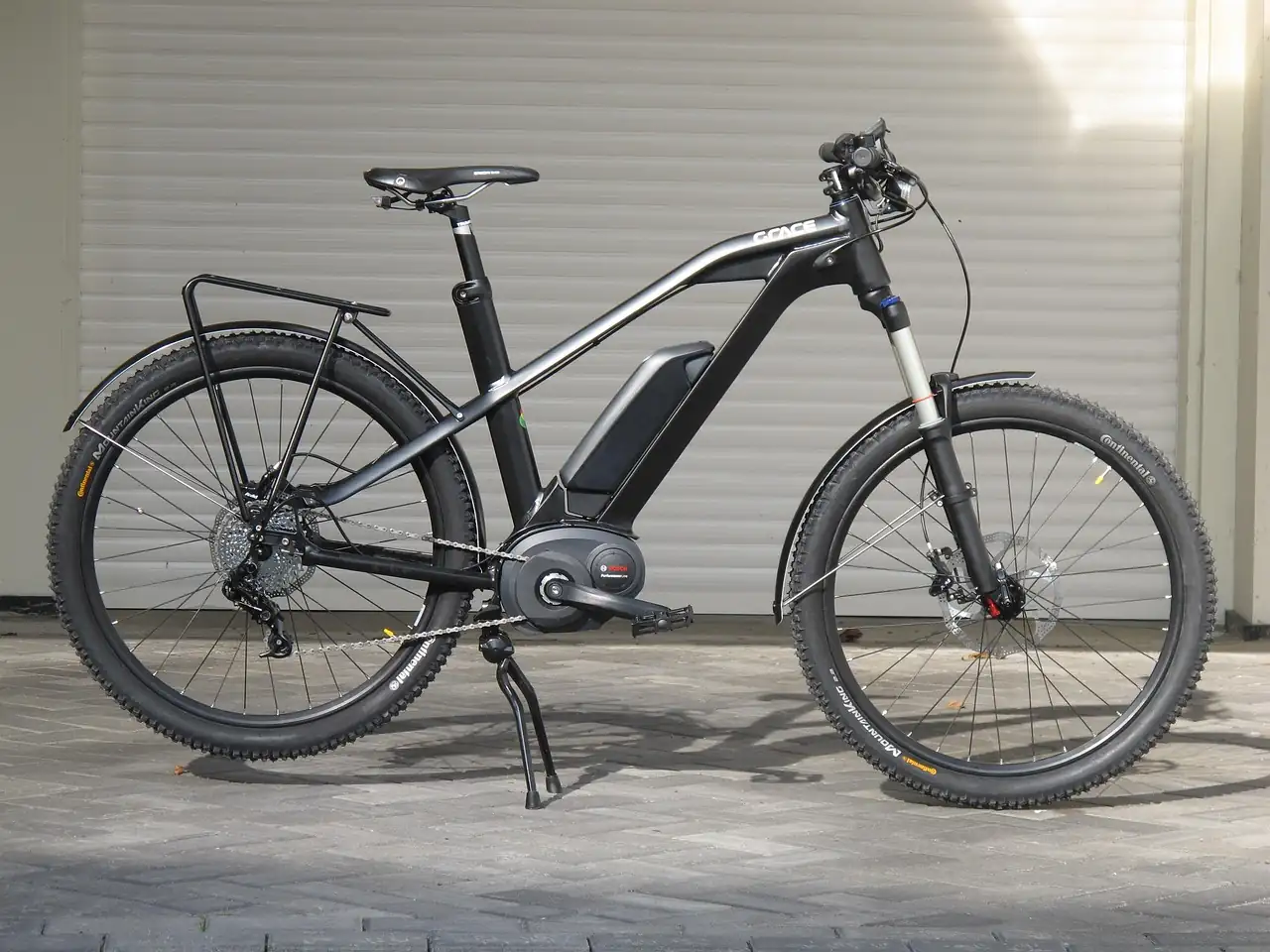 Vélo électrique noir avec batterie intégrée au cadre et moteur central, garé devant un rideau métallique