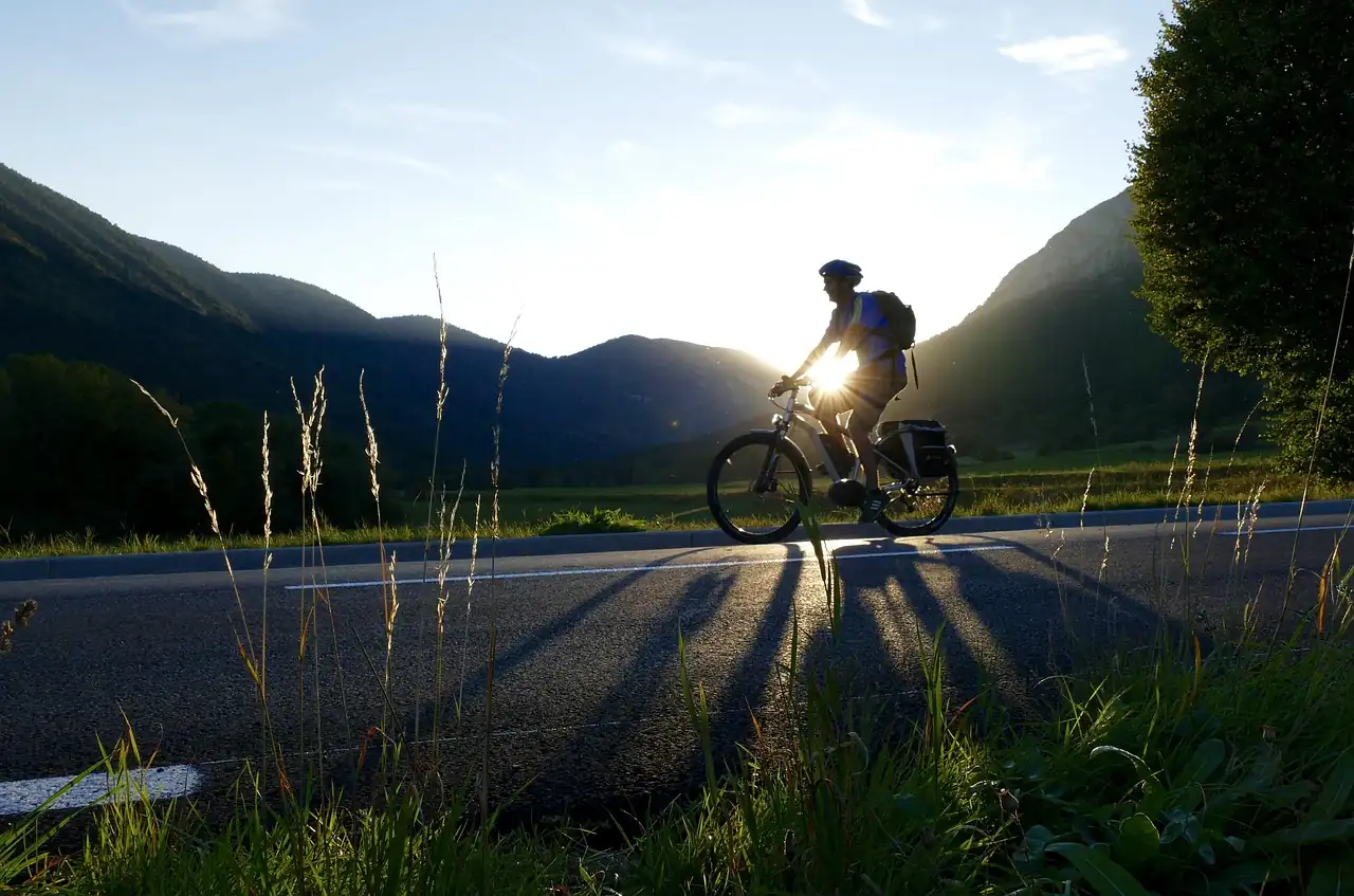 Cycliste casqué sur un vélo électrique à sacoches, sur une route de vallée au coucher du soleil