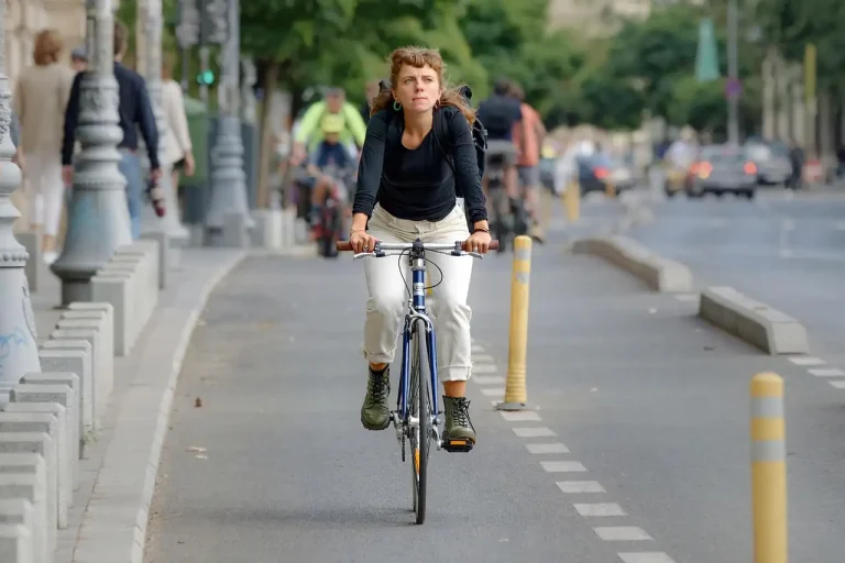 Cycliste en pantalon clair sur une piste cyclable séparée de la chaussée par des bordures et des potelets jaunes