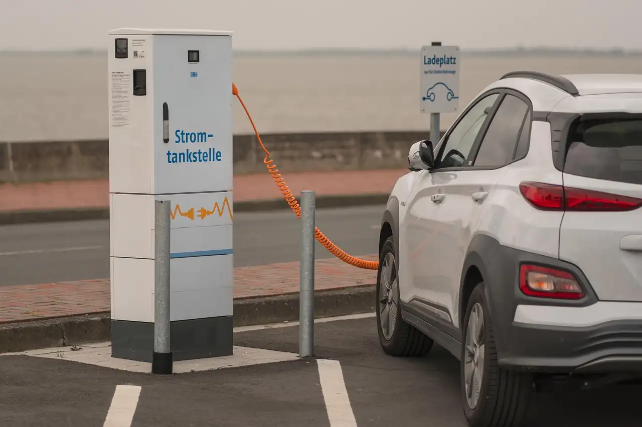 Voiture électrique blanche branchée par un câble orange spiralé à une borne de recharge en bord de mer
