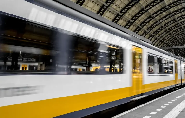 Train de voyageurs blanc et jaune en mouvement le long du quai sous la verrière métallique de la gare