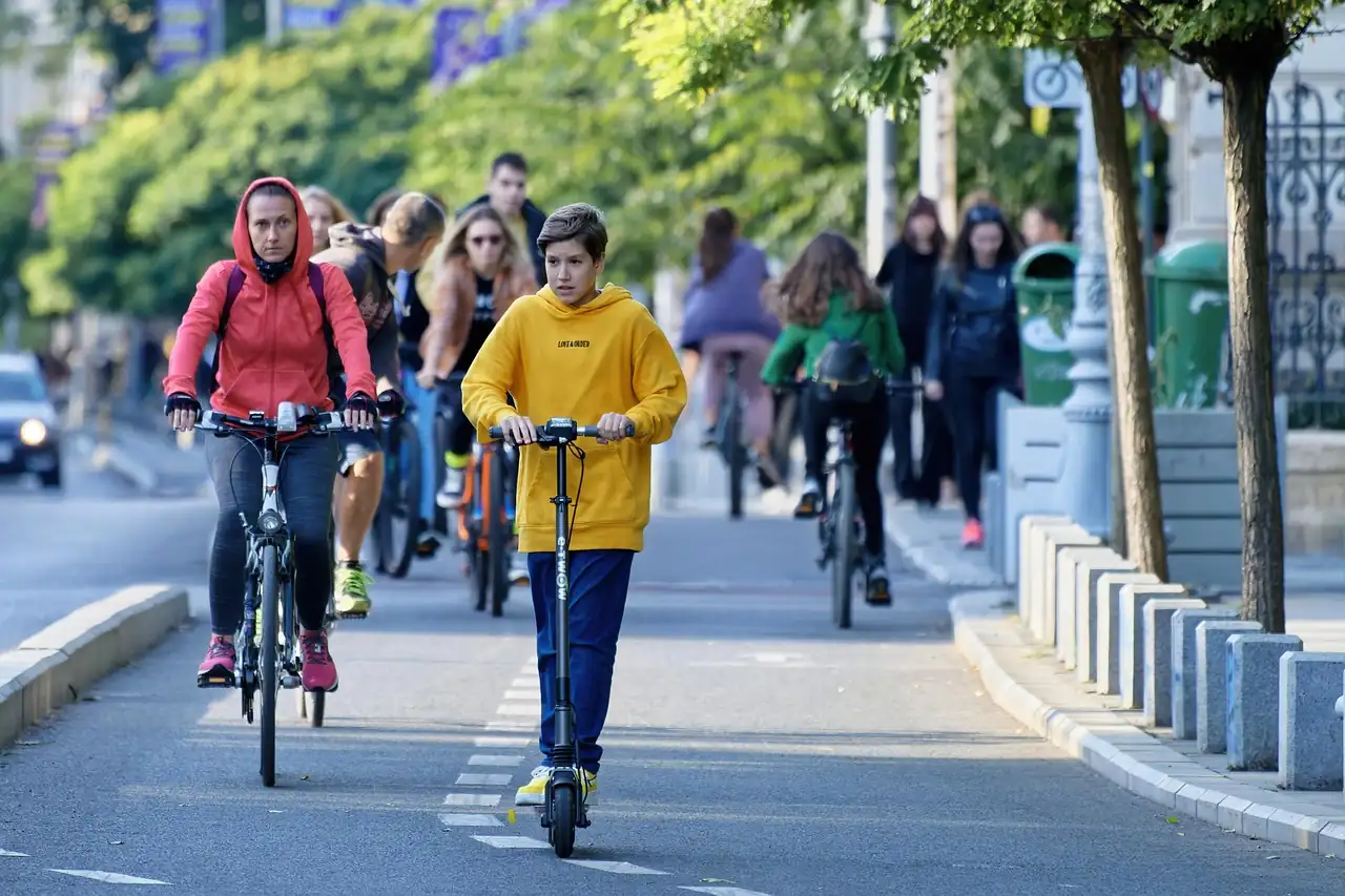 Adolescent en trottinette électrique sans casque sur une piste cyclable, entouré de cyclistes