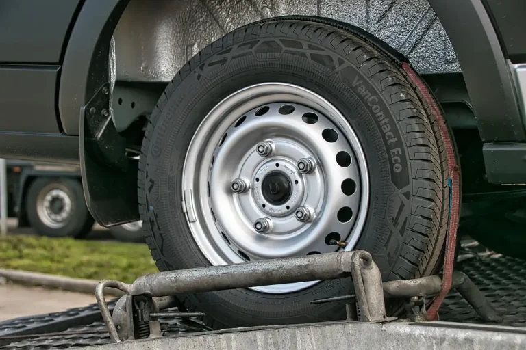 Roue arrière de voiture maintenue par une sangle rouge sur un plateau de dépanneuse