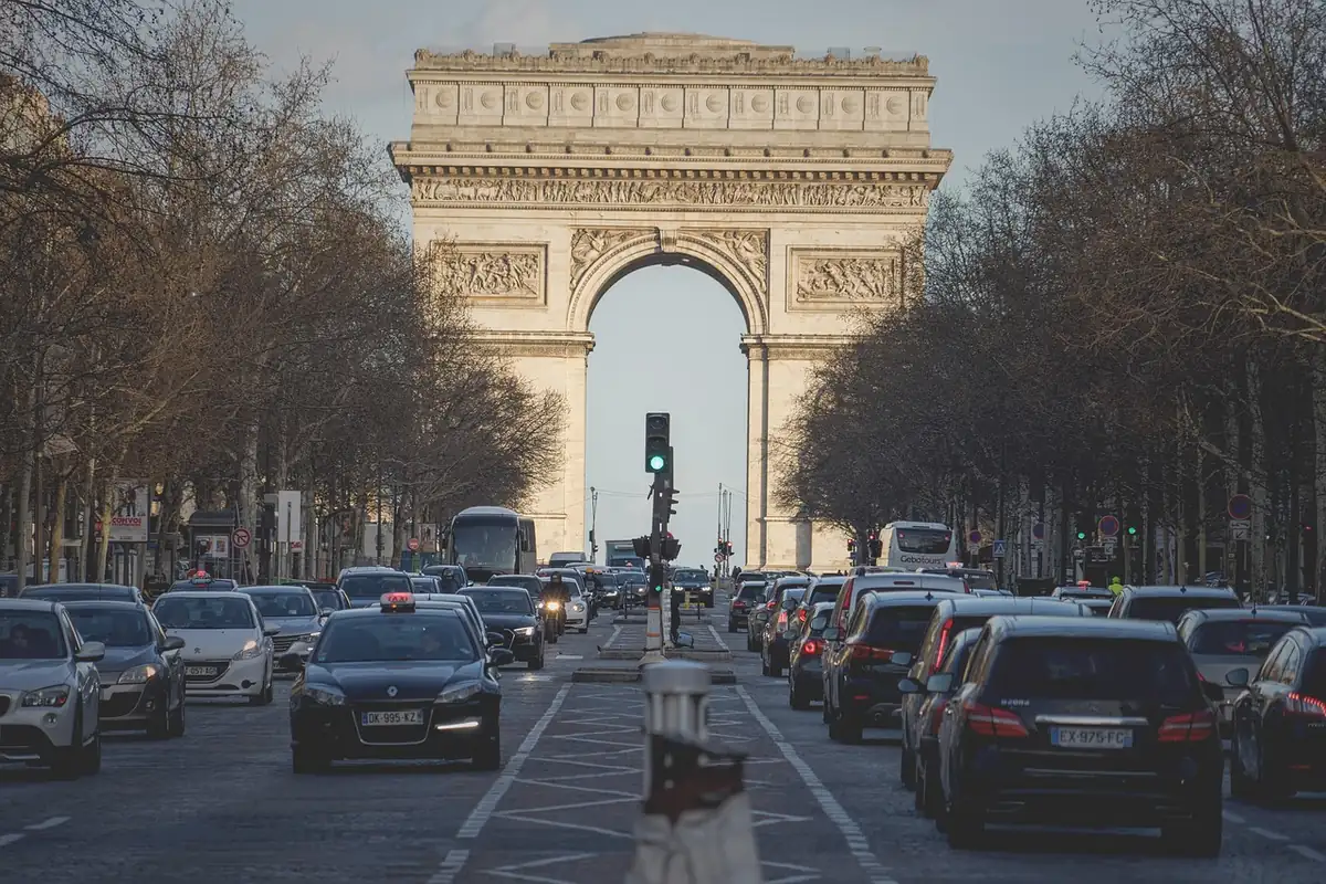 Files de voitures et un taxi à l'arrêt sur les Champs-Élysées, l'Arc de Triomphe au fond, feu au vert