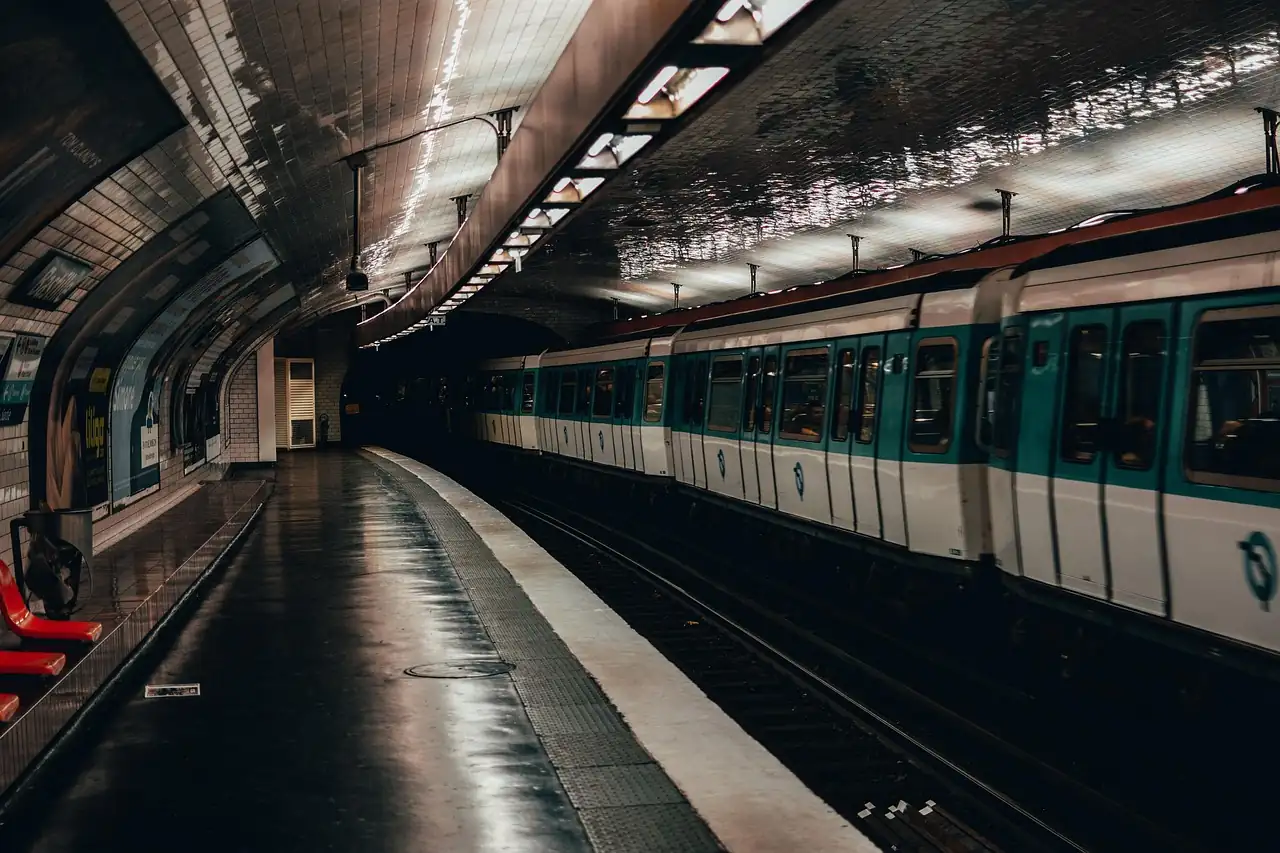 Rame de métro parisien blanche et verte à quai dans une station voûtée, sièges rouges au premier plan