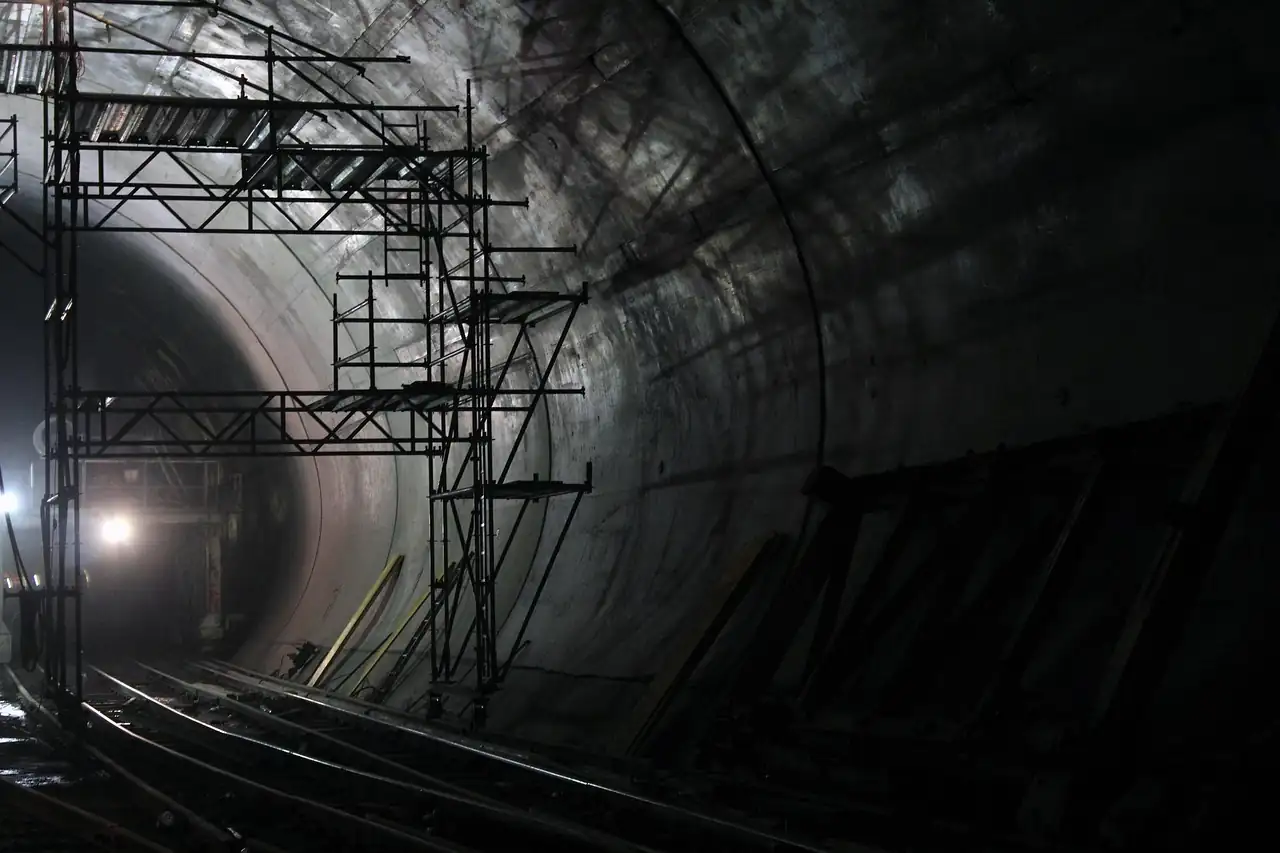Tunnel ferroviaire en construction, parois de béton brut, échafaudages métalliques et rails posés au sol