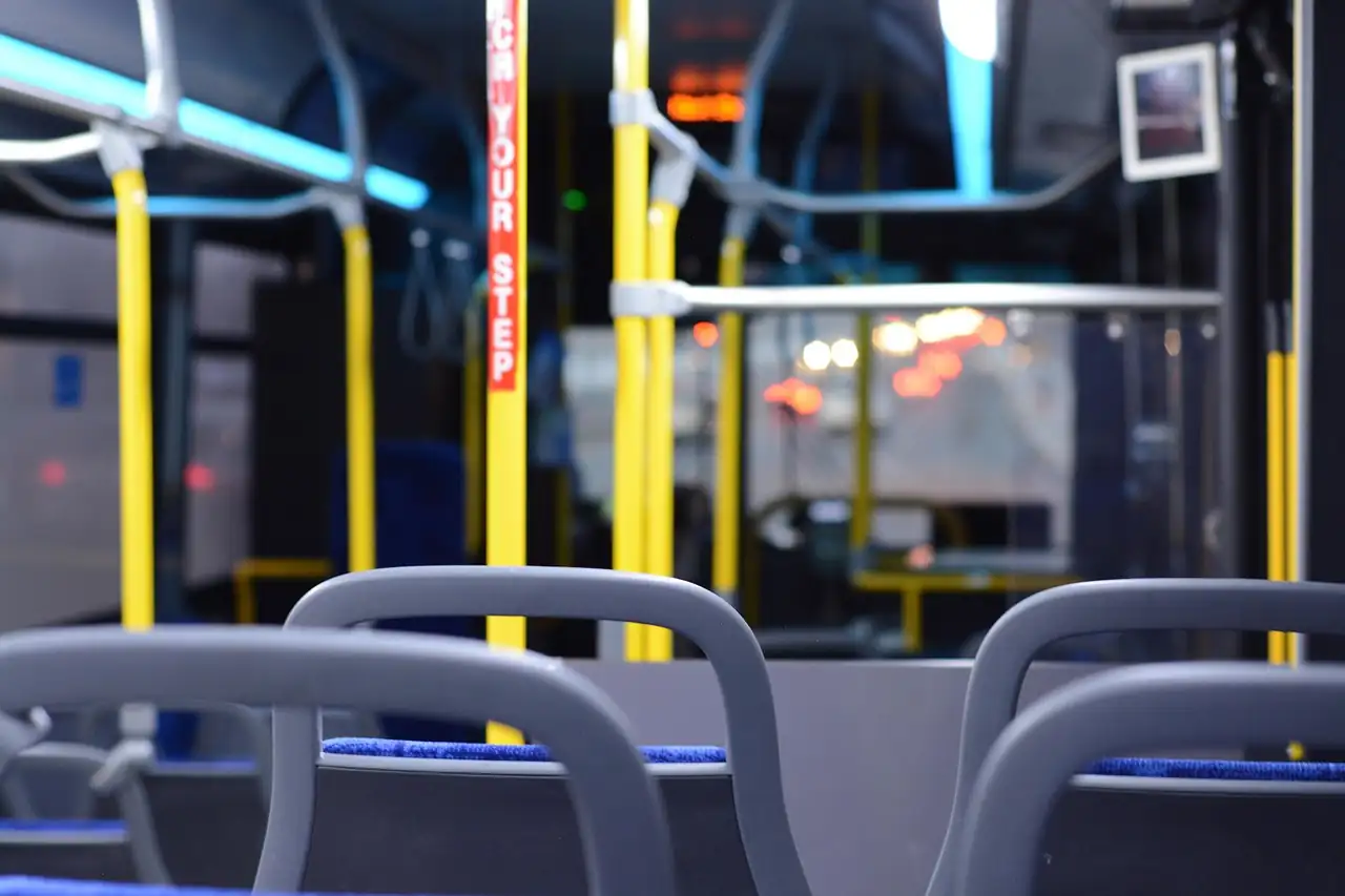 Intérieur d'un bus vide de nuit, sièges gris et bleus au premier plan, barres jaunes et feux de la ville flous derrière