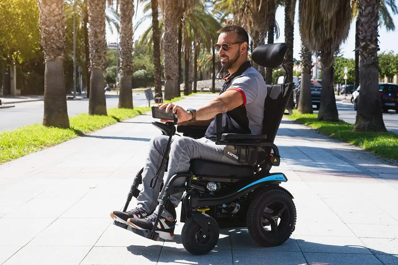 Homme en fauteuil roulant électrique sur un trottoir bordé de palmiers, voitures garées le long de l'avenue