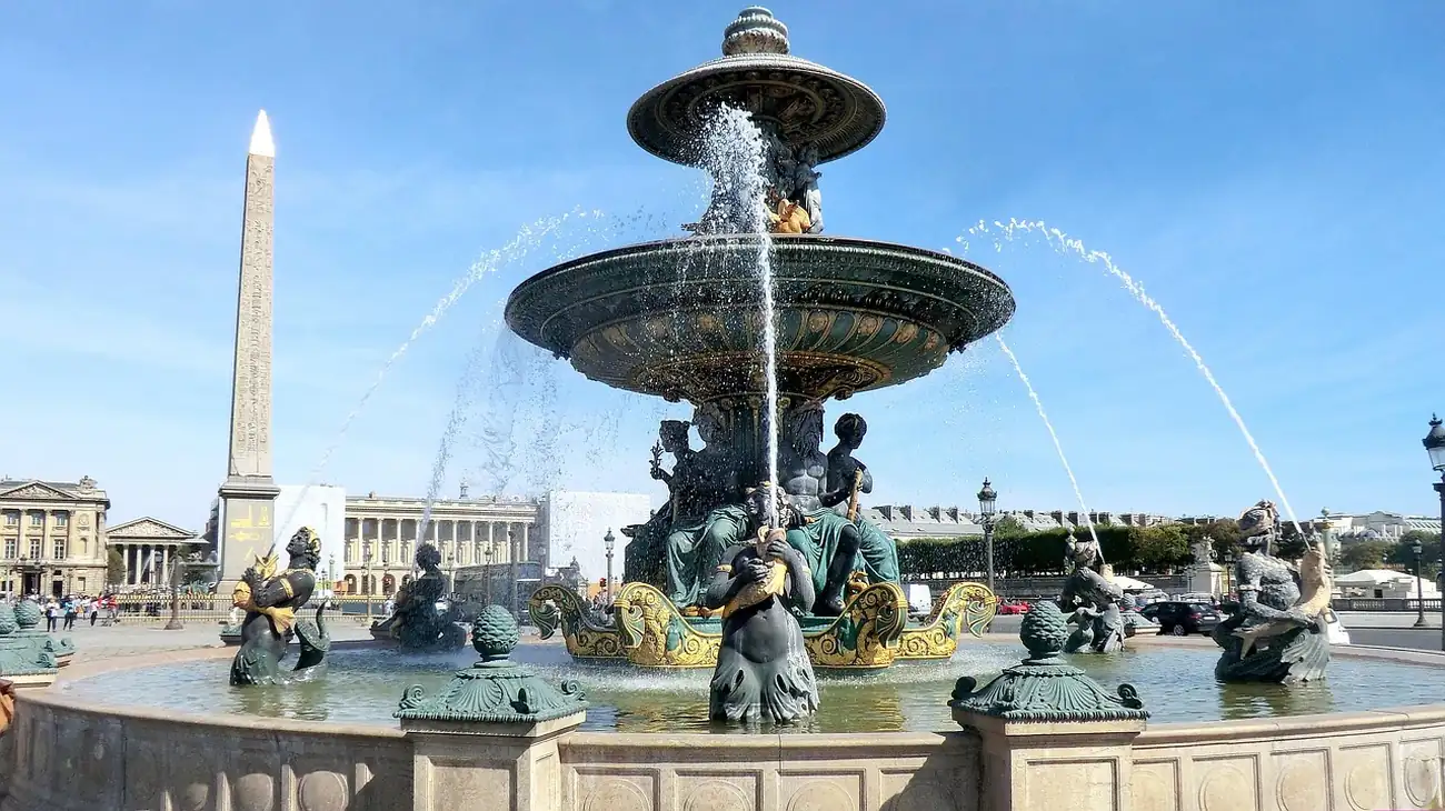 Fontaine des Mers en bronze vert et or place de la Concorde, l'obélisque de Louxor derrière sous un ciel bleu