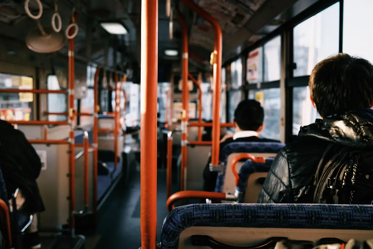 Intérieur de bus vu de la dernière rangée, barres orange et passagers assis face à la route