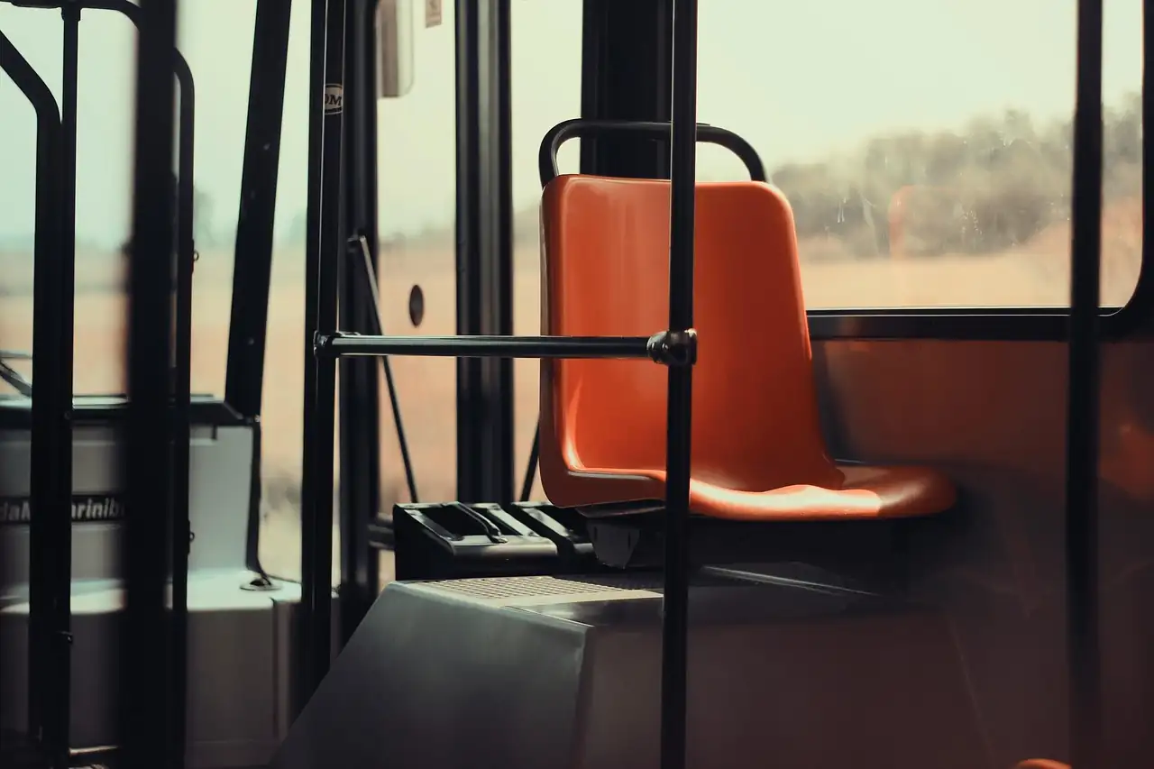 Siège en plastique orange vide dans un bus, la campagne défilant derrière la vitre