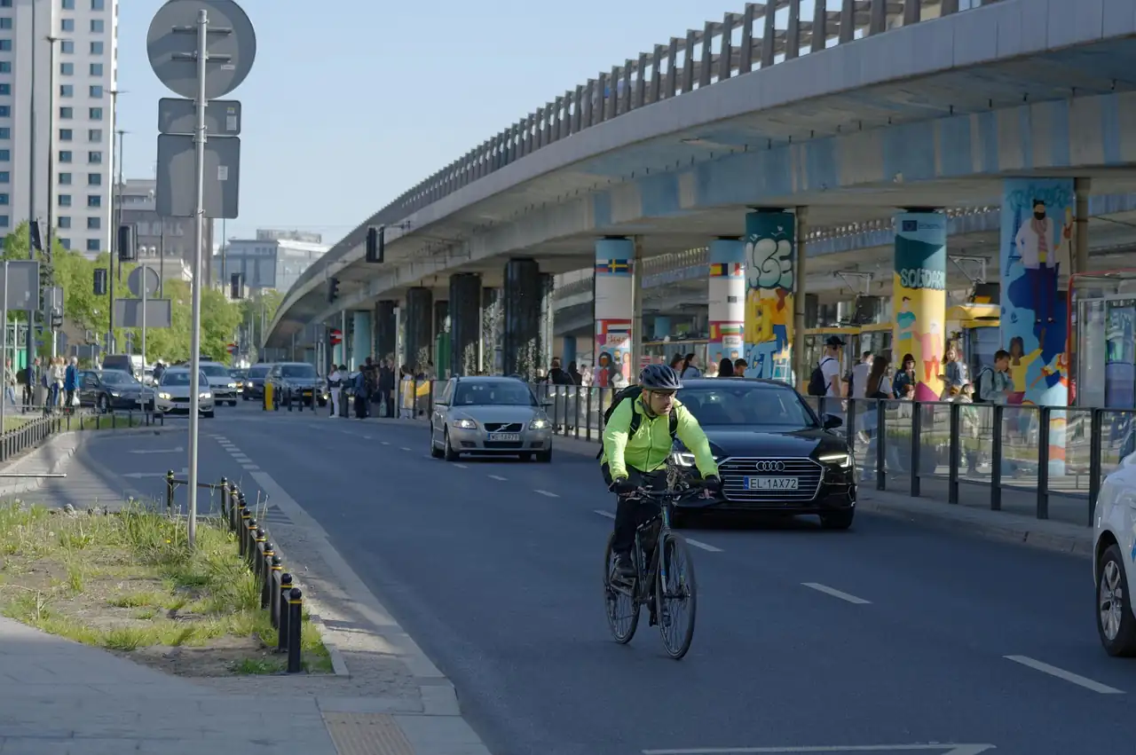 Cycliste en veste fluo roulant sur la chaussée entre les voitures, sous un viaduc routier en béton