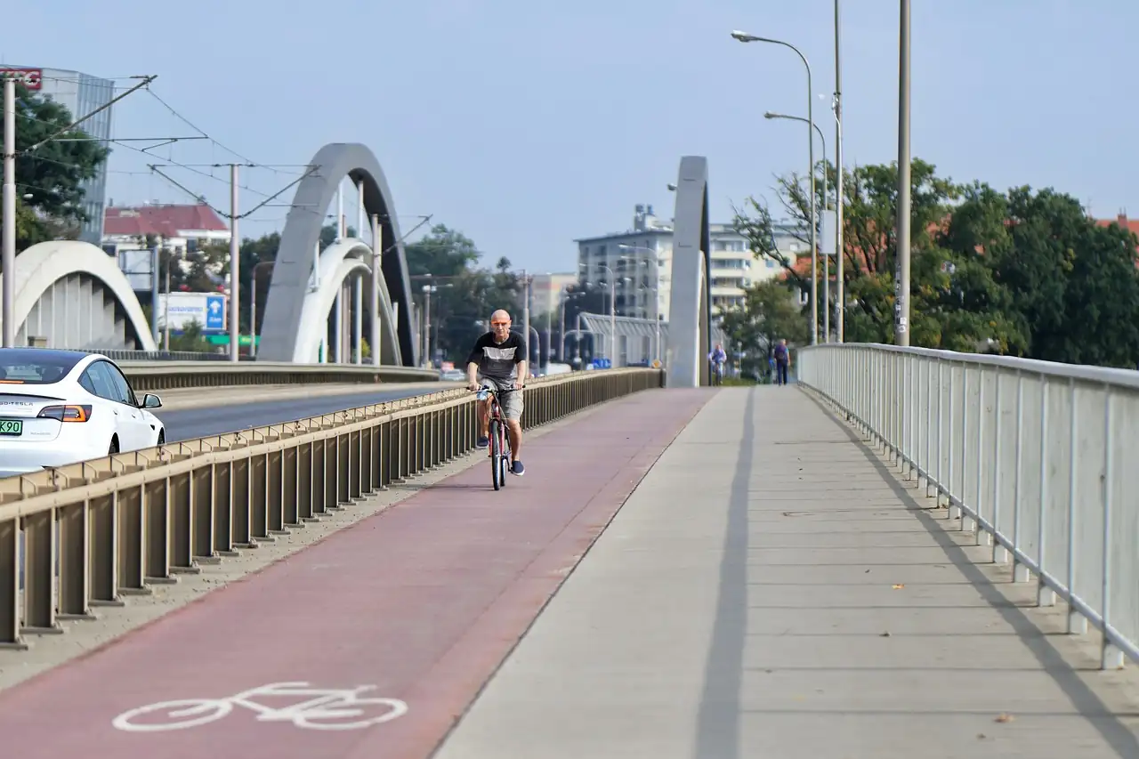 Cycliste seul sur la piste cyclable rouge d'un pont routier, séparé des voitures par une glissière, arches au fond
