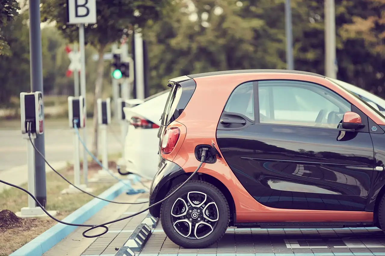 Citadine électrique orange et noire branchée à une borne de recharge sur un parking en ville