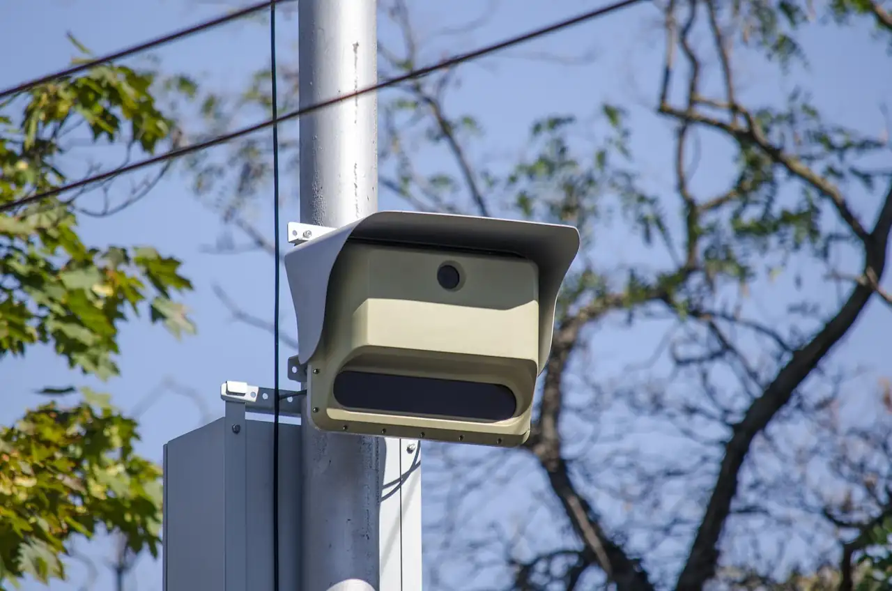 Caméra de surveillance routière fixée sur un poteau métallique, arbres en arrière-plan