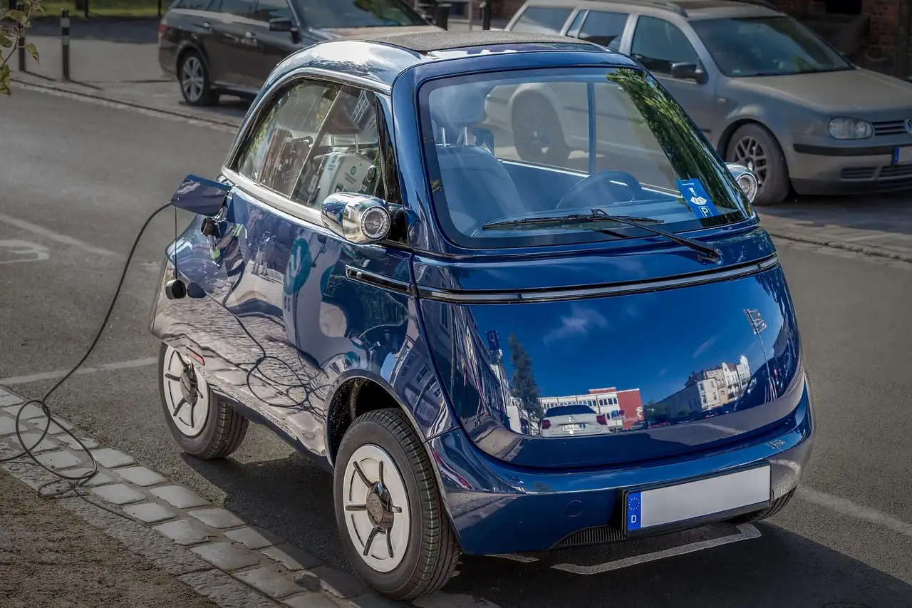 Microlino bleue branchée sur une prise de recharge, garée le long du trottoir en ville