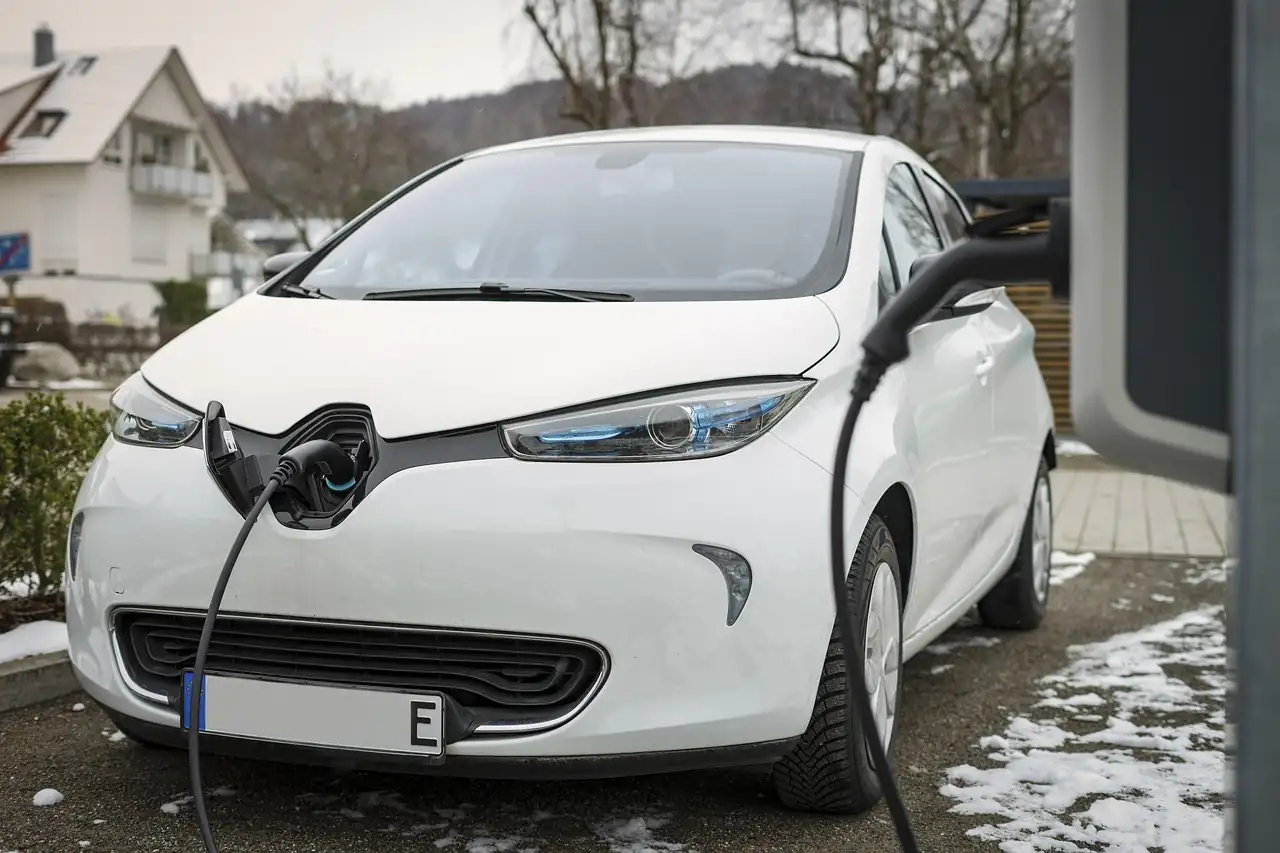 Renault Zoé blanche branchée à une borne devant une maison, neige sur le sol