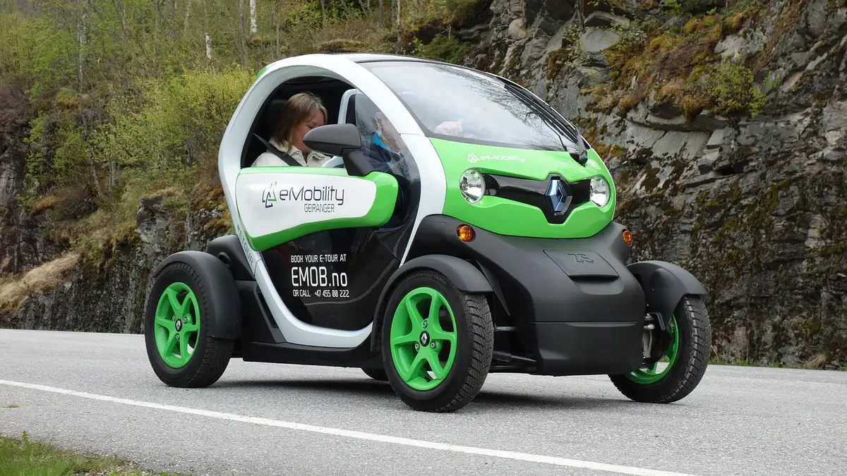 Renault Twizy vert et blanc roulant sur une route de montagne, une conductrice à bord