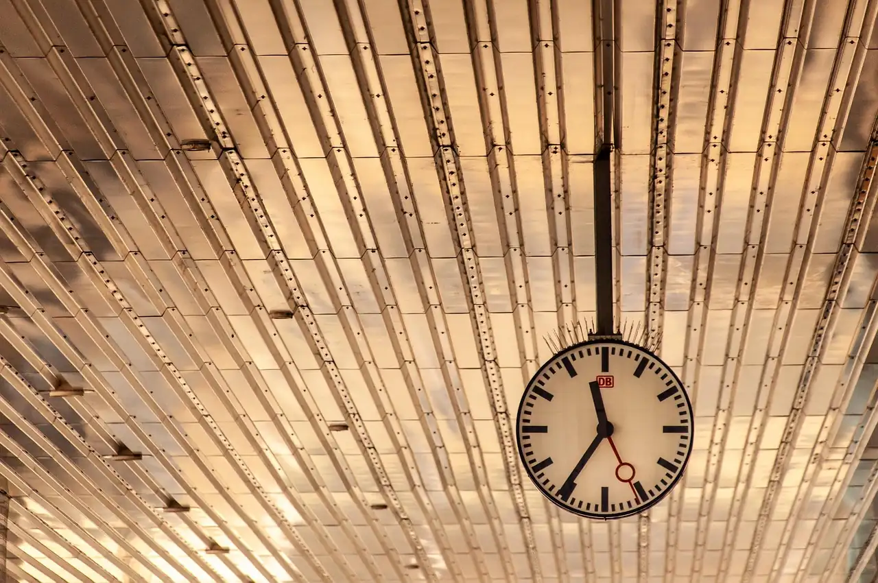 Horloge de gare ronde suspendue sous un plafond métallique doré à lattes