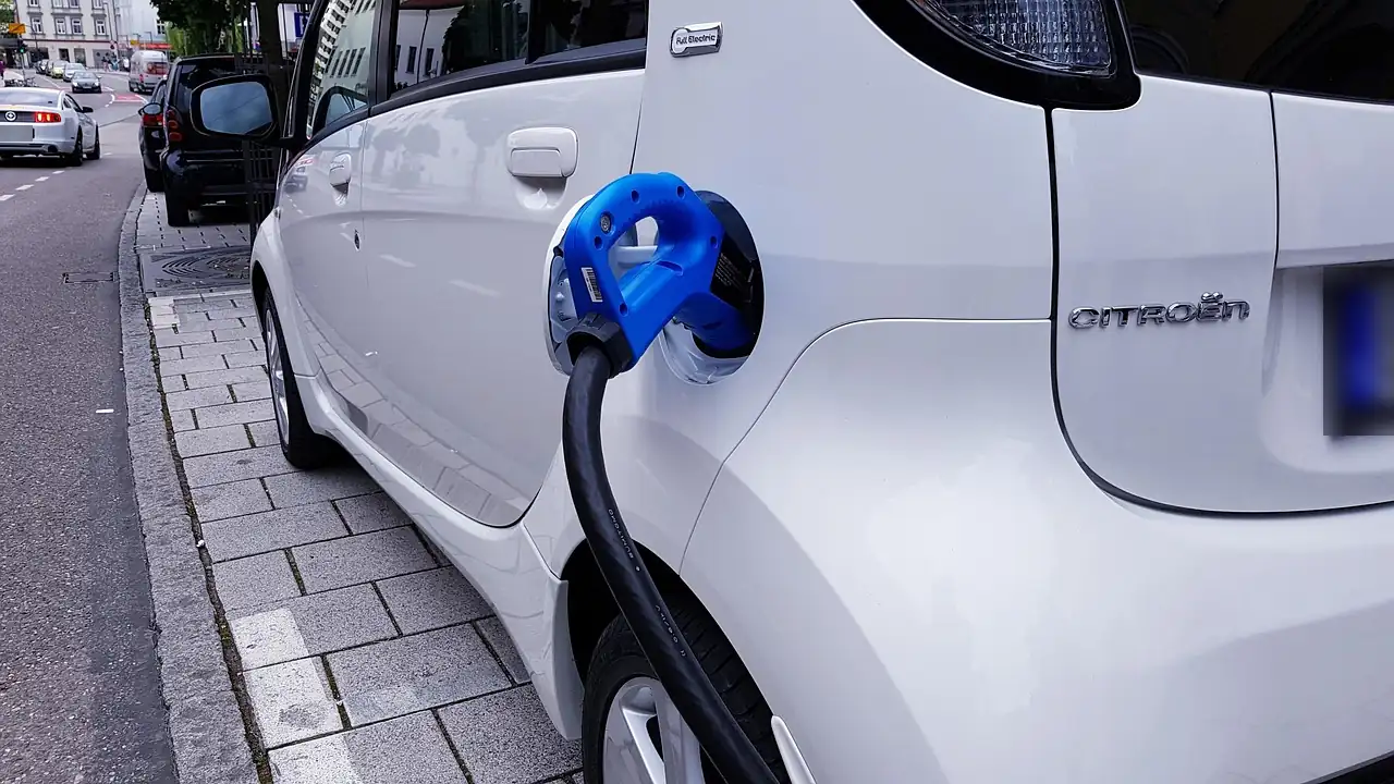 Petite citadine électrique Citroën blanche branchée par un câble bleu, garée le long du trottoir pavé