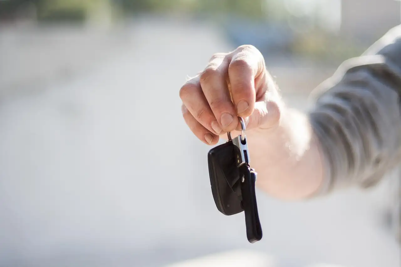 Main tendant une clé de voiture noire sur fond clair et flou, comme lors de la remise des clés