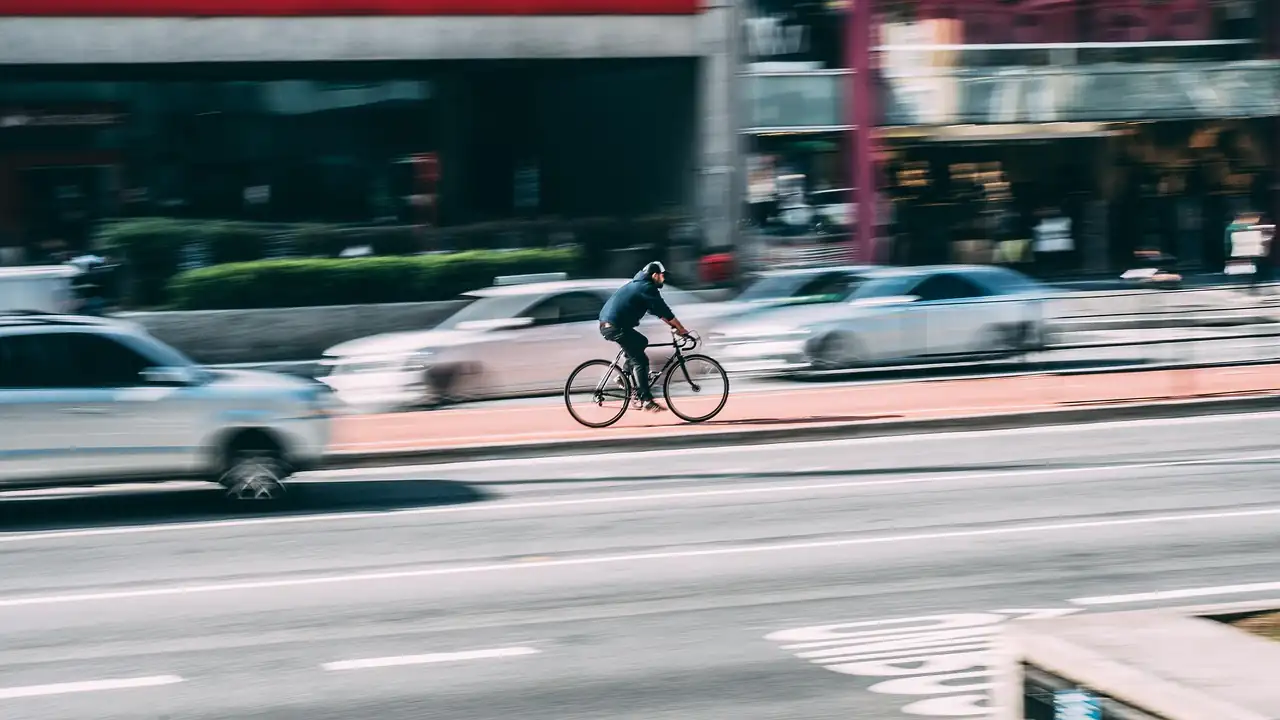Cycliste roulant sur une bande cyclable rouge au milieu de voitures floues en mouvement