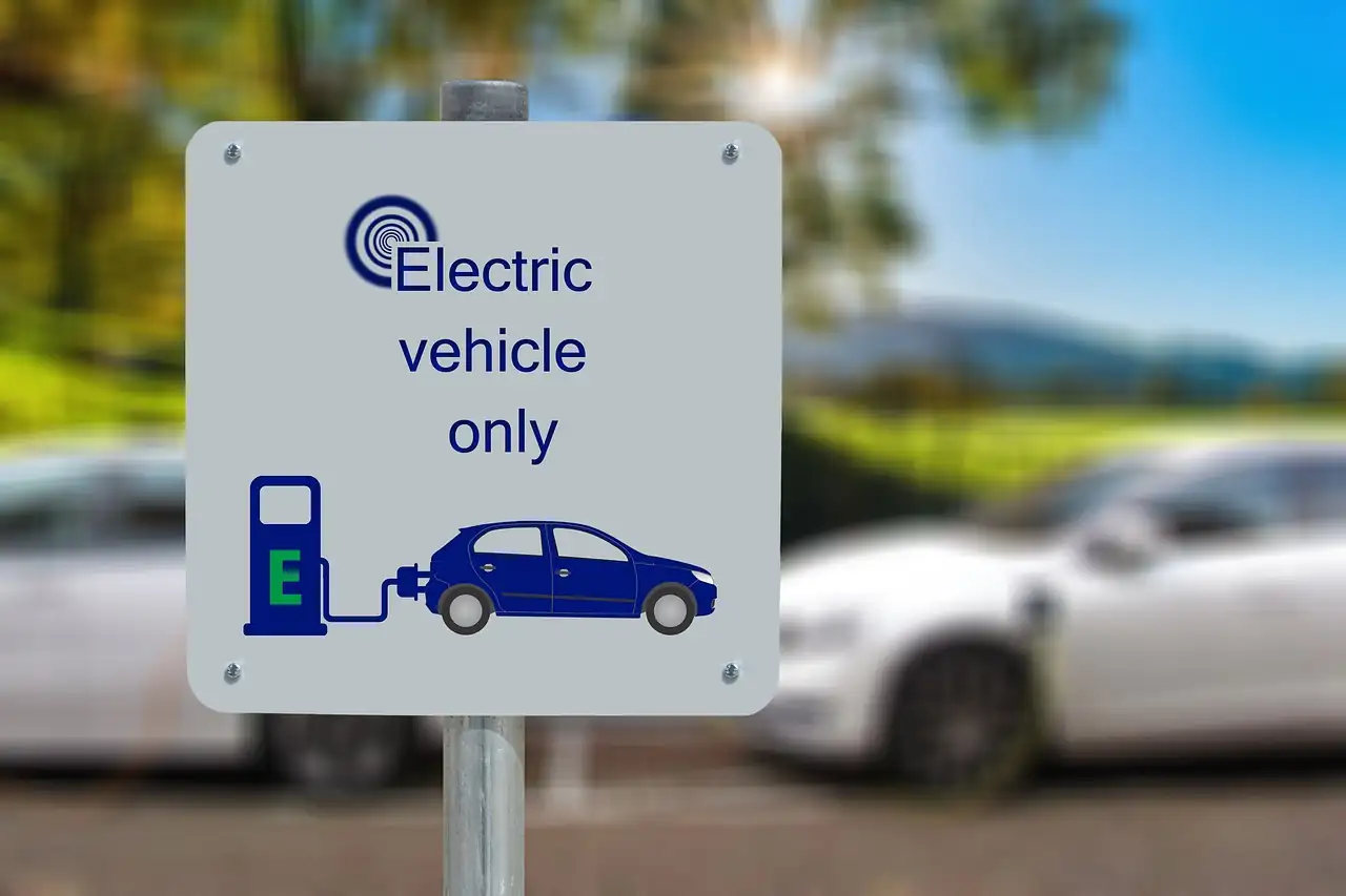 Panneau de stationnement réservé aux véhicules électriques devant des voitures blanches floues