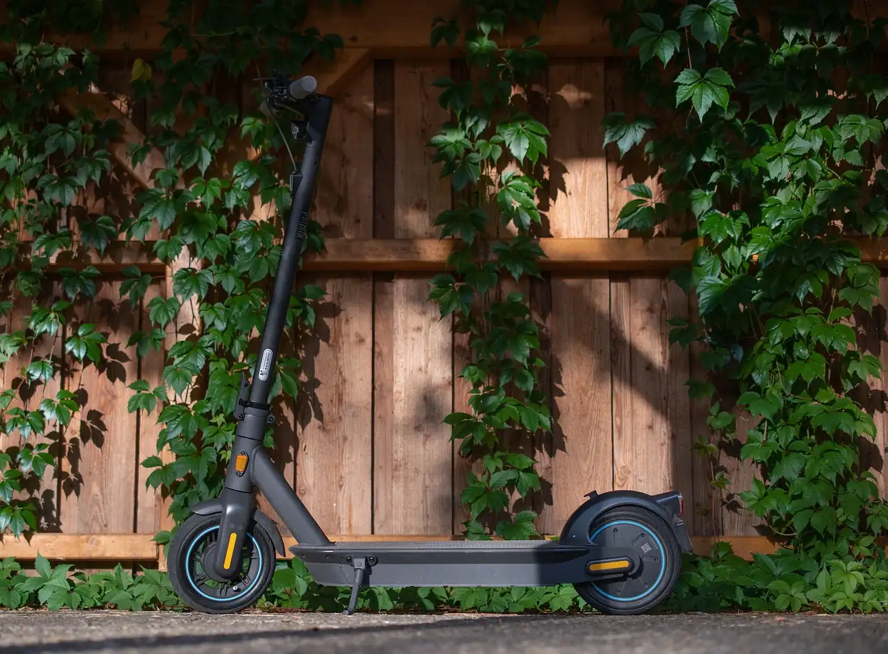 Trottinette électrique noire à deux roues garée devant une palissade en bois couverte de vigne vierge